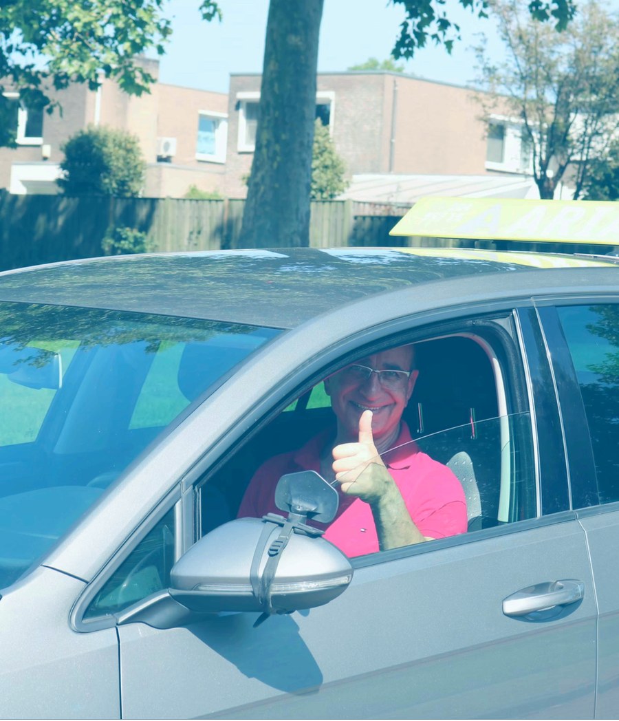 Instructeur van Rijschool Aria geeft een duim omhoog vanuit de lesauto